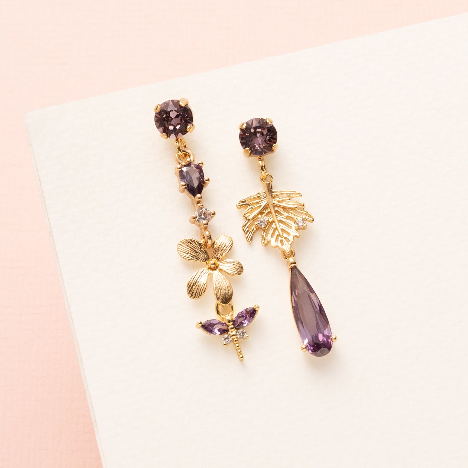 Laat je betoveren door de natuurlijke elegantie van de Lavender Garden asymmetrische oorbellen. De oorbel heeft paarse Swarovski oorstekers, een paars zirkonia tussenstuk en een delicate bloem, waaraan een paarse libelle gracieus hangt. De andere oorbel is voorzien van een gouden blaadje met zirkonia steentjes en een paarse druppel, wat het asymmetrische ontwerp extra speels en verfijnd maakt. Perfect voor een etentje, een feestje of een speciale gelegenheid, en een subtiel statement dat je vrouwelijke en e