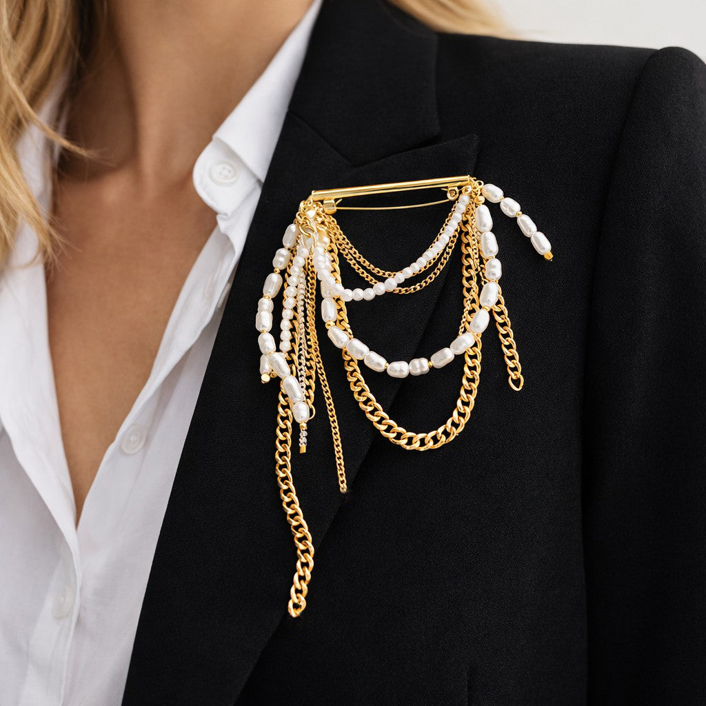 Deze goudkleurige statement broche met speelse kettinkjes en verschillende imitatie parels is een echte eye-catcher. Groot, opvallend en vrouwelijk, met een perfecte balans tussen chique elegantie en stoere uitstraling. Draag haar op een blazer, jas of sjaal en geef elke outfit direct karakter en power.