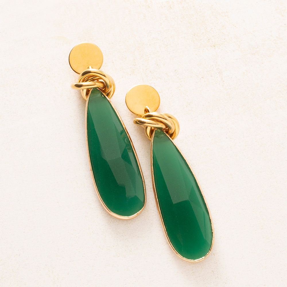 Verde Twist combineert strak goud met een diepe, rijke kleur Groen. Aan een glad gouden oorsteker hangt een knoop van in elkaar gevlochten ringen, gevolgd door een lange, facetgeslepen druppel in diepgroen. De dunne gouden rand geeft de steen een verfijnde afwerking.
Het is een tijdloos ontwerp met karakter: de knoop zorgt voor stoerheid, de druppel voor elegantie.