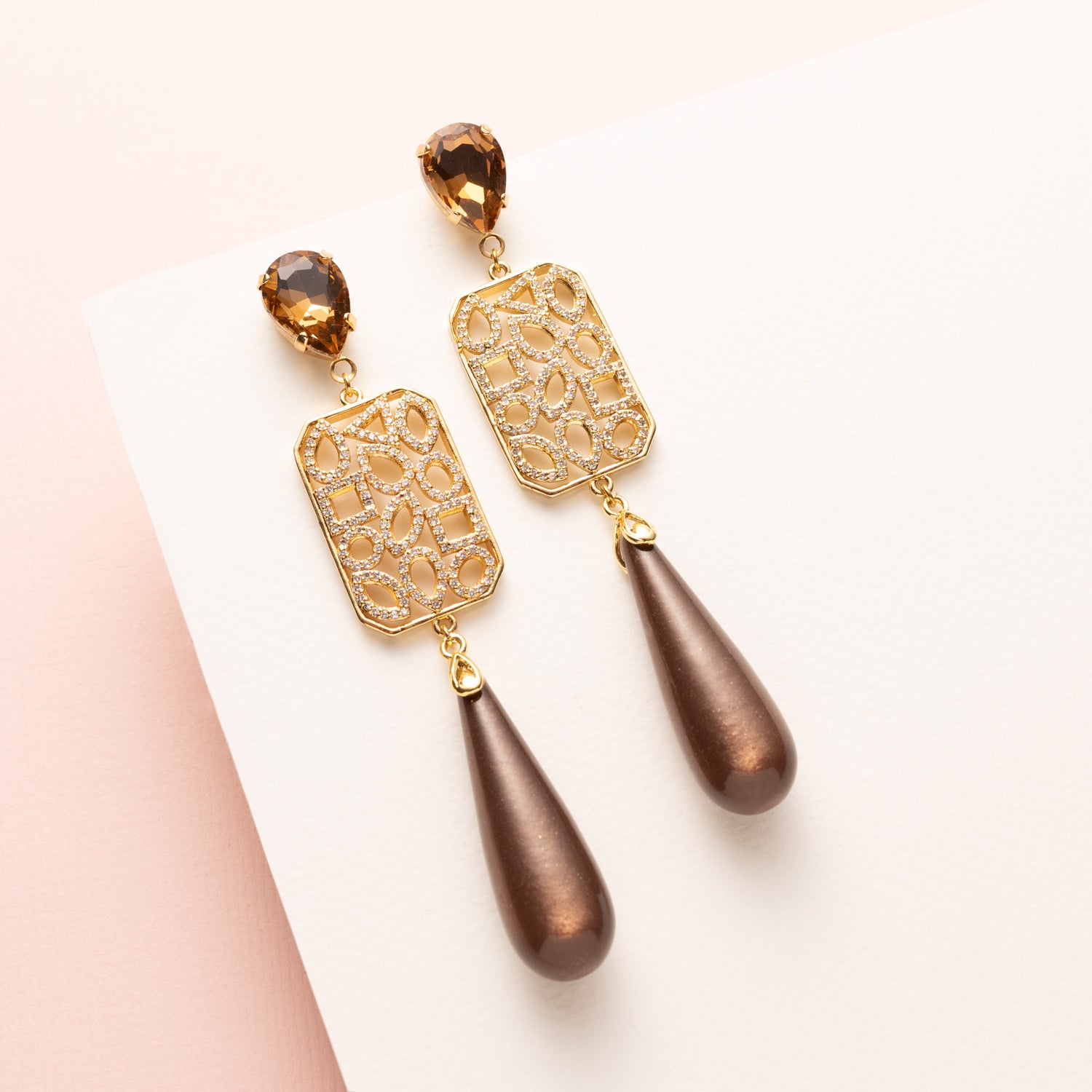 Grand Allure is een spectaculaire statement oorbel die luxe, elegantie en de bruine trendkleur perfect combineert. Kies zelf je stijl met een ronde Swarovski oorsteker of druppelvormige Strass oorsteker in Light Smoked Topaz. Het grote, rechte tussenstuk is versierd met verschillende vormen zirkonia steentjes, en daaronder hangt een glanzende donkerbruine Polaris druppel.
Een oorbel die kracht, glamour en impact uitstraalt – een echte eyecatcher voor vrouwen die durven op te vallen.