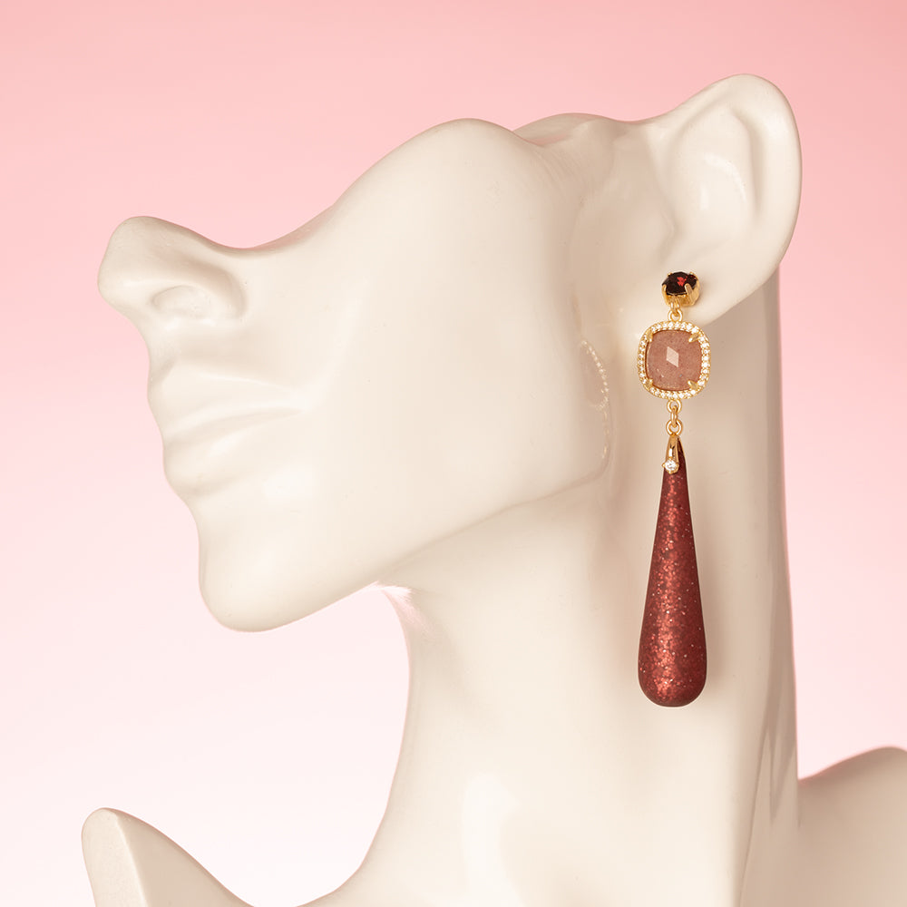 Elegante grote oorbellen, ontworpen om op te vallen. De oorstekers zijn bezet met een schitterende Swarovski puntsteen in de kleur burgundy, terwijl de donkerrode Polaris druppels een diepe, warme gloed toevoegen. De natuurlijke schoonheid van aardbeienkwarts maakt het ontwerp compleet, met een vleugje luxe en verfijning.