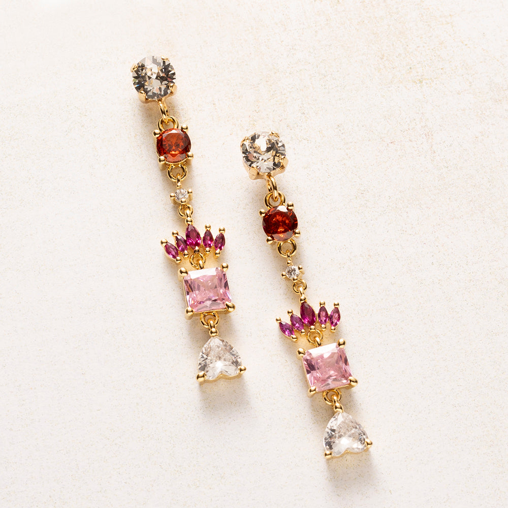 Royal Blush is een kleine verzameling juwelen in één oorbel. Onder een fonkelende Swarovski oorsteker volgen zirkonia steentjes in warm rood, fuchsia en zacht roze. Een kroontje van marquise-geslepen steentjes rust boven een vierkante roze steen, en een helder hartje vormt het slotstuk.
De kleuren lopen van diep naar licht, en de gouden zetting houdt alles verfijnd. Deze oorbellen staan mooi bij een eenvoudige outfit, maar net zo goed bij een feestelijke look.