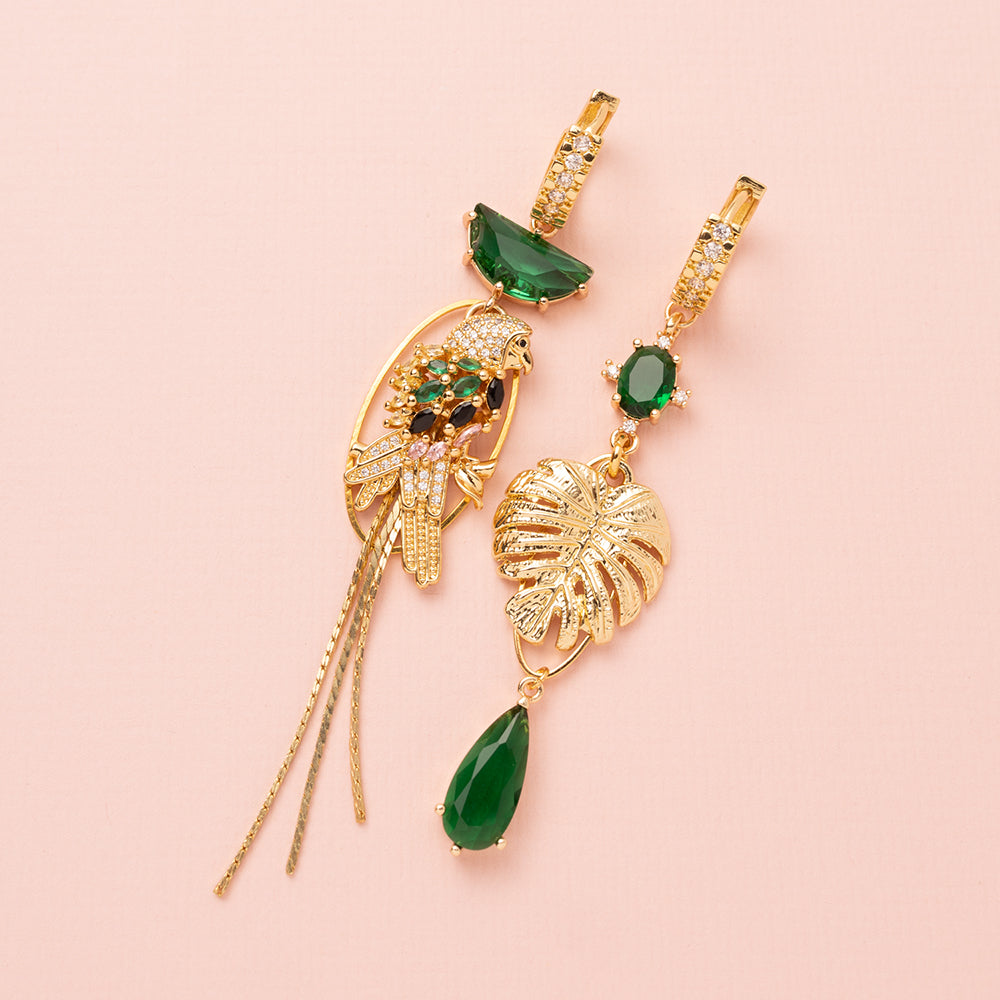 Asymmetrische statement oorbellen met een papegaai en een monstera blad. Met zirkonia oorringen en zirkonia bedels in de kleuren goud en groen