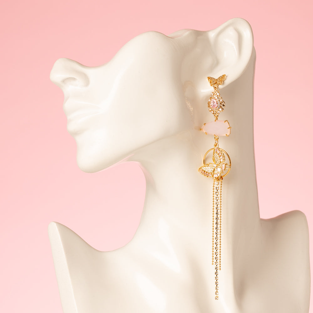 Asymmetrische statement oorbellen met zirkonia vlinder oorstekers. Een mix van glanzende en mat roze stenen en een roze vlinder