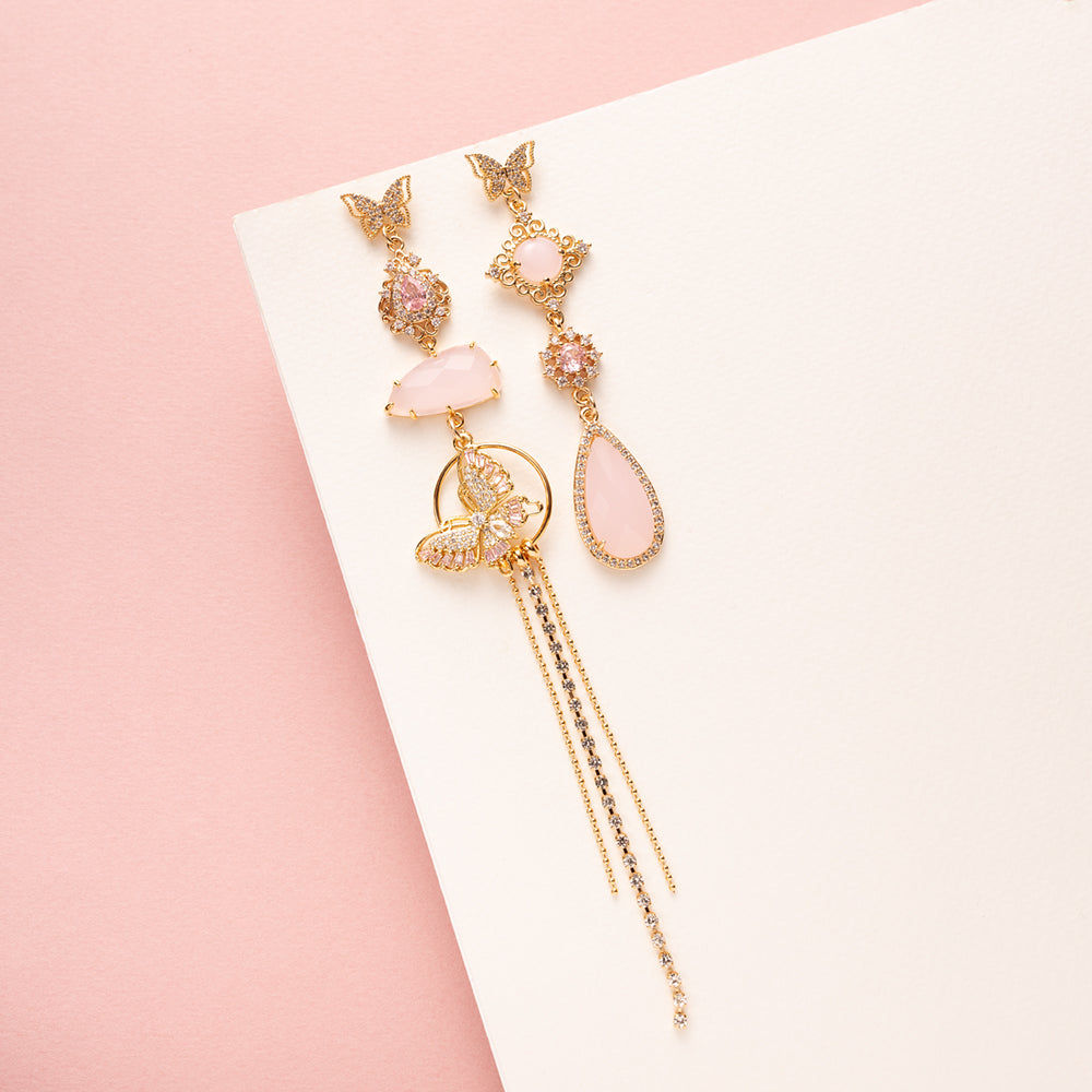 Asymmetrische statement oorbellen met zirkonia vlinder oorstekers. Een mix van glanzende en mat roze stenen en een roze vlinder