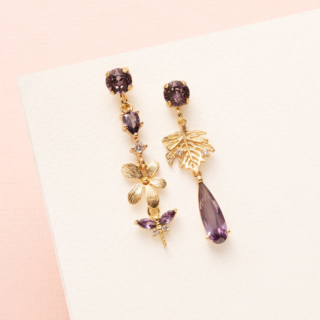Laat je betoveren door de natuurlijke elegantie van de Lavender Garden asymmetrische oorbellen. De oorbel heeft paarse Swarovski oorstekers, een paars zirkonia tussenstuk en een delicate bloem, waaraan een paarse libelle gracieus hangt. De andere oorbel is voorzien van een gouden blaadje met zirkonia steentjes en een paarse druppel, wat het asymmetrische ontwerp extra speels en verfijnd maakt. Perfect voor een etentje, een feestje of een speciale gelegenheid, en een subtiel statement dat je vrouwelijke en e