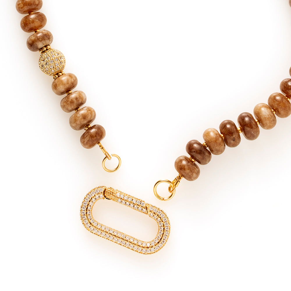 Earth Essence – Signature Clasp is uitgevoerd met dezelfde warme bruine natuursteen kralen. De tint is diep en natuurlijk, waardoor de ketting moeiteloos combineert met zowel lichte als donkere outfits.

Het verschil zit in het zirkonia slot. Deze variant heeft een ander type sluiting (veersluiting) dat een eigen uitstraling geeft: groot, sprankelend en opvallend als designaccent. Het slot fungeert niet alleen als sluiting, maar ook als stijlvol detail dat gezien mag worden.