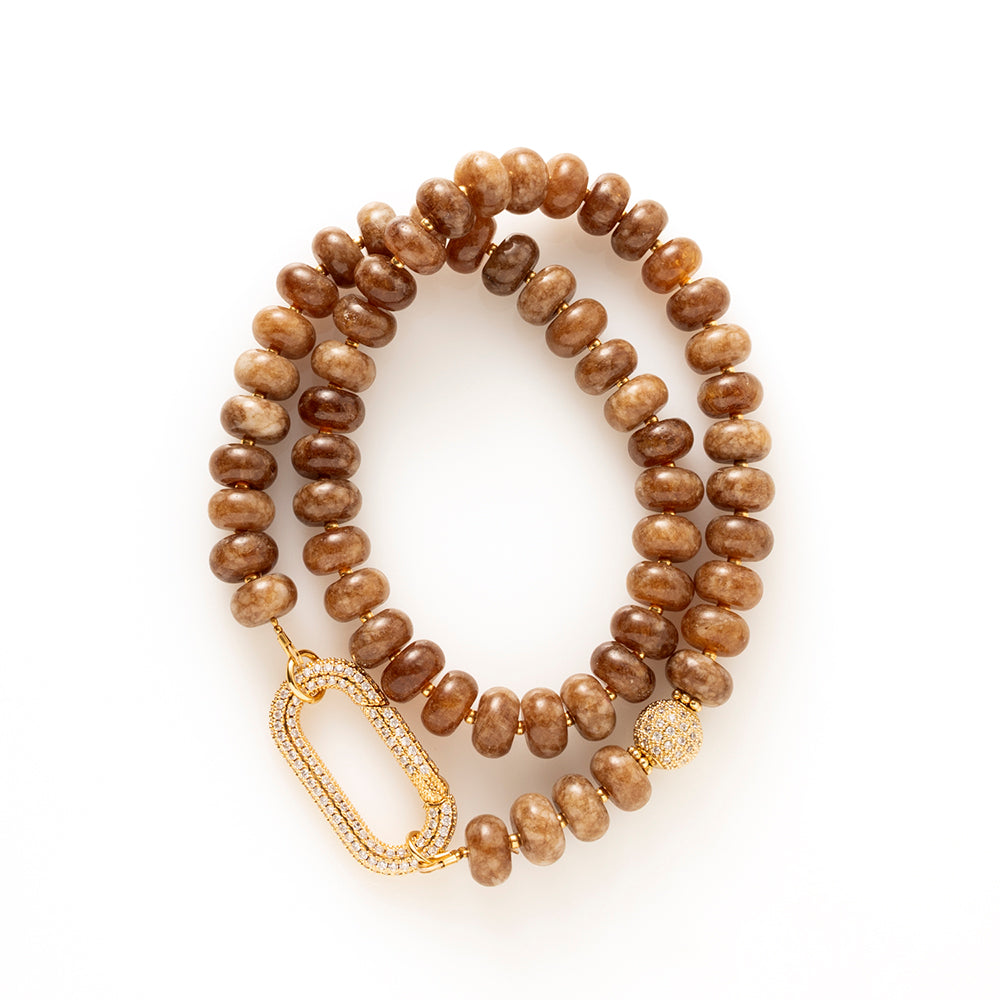 Earth Essence – Signature Clasp is uitgevoerd met dezelfde warme bruine natuursteen kralen. De tint is diep en natuurlijk, waardoor de ketting moeiteloos combineert met zowel lichte als donkere outfits.

Het verschil zit in het zirkonia slot. Deze variant heeft een ander type sluiting (veersluiting) dat een eigen uitstraling geeft: groot, sprankelend en opvallend als designaccent. Het slot fungeert niet alleen als sluiting, maar ook als stijlvol detail dat gezien mag worden.