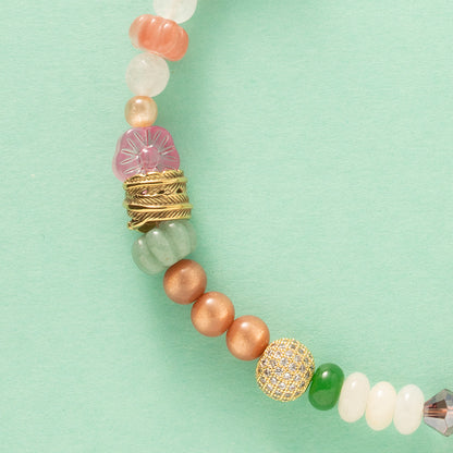 Laat je meevoeren in een dromerige zomerwereld met Wildflower Dreams, een handgemaakte statement ketting in kleurrijke boho-stijl. Deze unieke ketting combineert grote natuursteen kralen, fonkelende zirkonia’s en glaskralen in warme tinten zoals groen, warm oranje, paars, roze en wit. De combinatie van natuurlijke materialen en sprankelende accenten geeft deze ketting een speelse én elegante uitstraling.