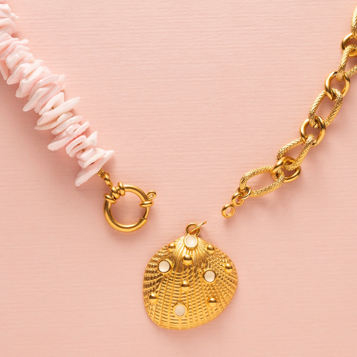 Ontdek de betoverende charme van deze ketting met schelp snippers in licht roze, aangevuld met een schitterende zirkonia kraal en een elegant boeislot aan de voorkant. Deze opvallende ketting bestaat uit twee delen: aan de ene kant delicaat gesneden schelp snippers en aan de andere kant een grove schakelketting, wat samen een trendy en elegante uitstraling creëert.