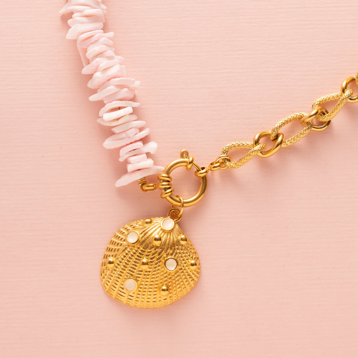 Ontdek de betoverende charme van deze ketting met schelp snippers in licht roze, aangevuld met een schitterende zirkonia kraal en een elegant boeislot aan de voorkant. Deze opvallende ketting bestaat uit twee delen: aan de ene kant delicaat gesneden schelp snippers en aan de andere kant een grove schakelketting, wat samen een trendy en elegante uitstraling creëert.