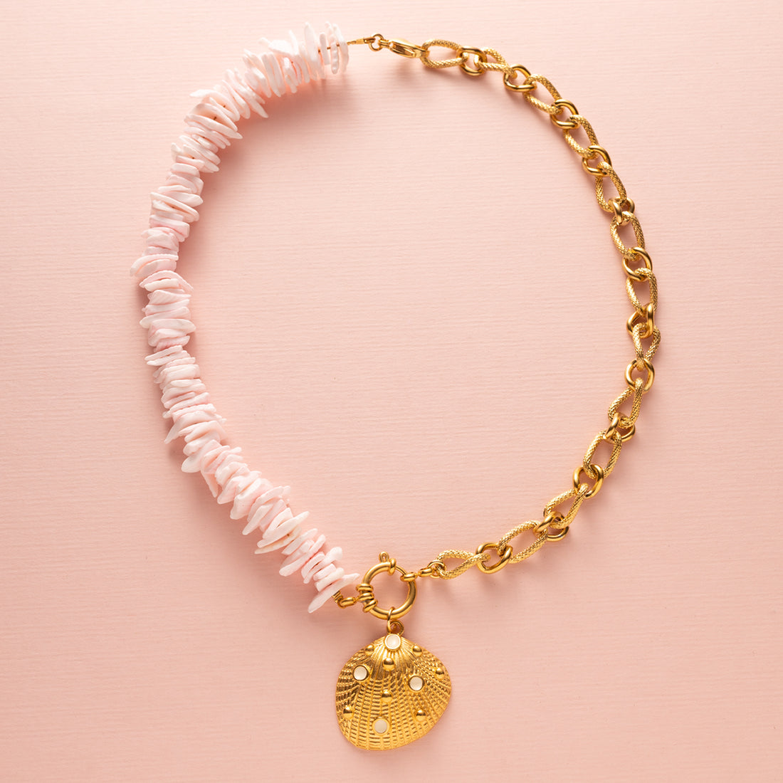 Ontdek de betoverende charme van deze ketting met schelp snippers in licht roze, aangevuld met een schitterende zirkonia kraal en een elegant boeislot aan de voorkant. Deze opvallende ketting bestaat uit twee delen: aan de ene kant delicaat gesneden schelp snippers en aan de andere kant een grove schakelketting, wat samen een trendy en elegante uitstraling creëert.
