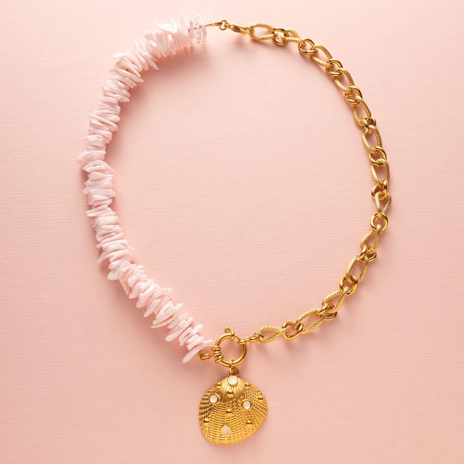 Ontdek de betoverende charme van deze ketting met schelp snippers in licht roze, aangevuld met een schitterende zirkonia kraal en een elegant boeislot aan de voorkant. Deze opvallende ketting bestaat uit twee delen: aan de ene kant delicaat gesneden schelp snippers en aan de andere kant een grove schakelketting, wat samen een trendy en elegante uitstraling creëert.