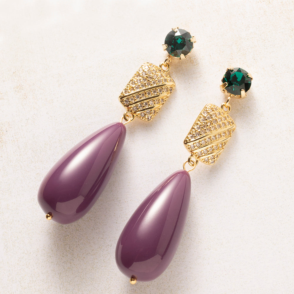 Een diepe aubergine druppel naast een smaragdgroen Swarovski kristal: een kleurcombinatie die opvalt zonder te schreeuwen. Het goudkleurige tussenstuk, bezet met zirkonia, vangt het licht bij elke beweging De gladde, glanzende druppel en de fonkelende steentjes maken deze oorbellen tegelijk verfijnd en krachtig.

Groot in formaat, rustig in kleur: verfijnd genoeg voor kantoor, opvallend genoeg voor een avondje uit.