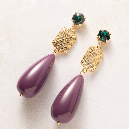 Een diepe aubergine druppel naast een smaragdgroen Swarovski kristal: een kleurcombinatie die opvalt zonder te schreeuwen. Het goudkleurige tussenstuk, bezet met zirkonia, vangt het licht bij elke beweging De gladde, glanzende druppel en de fonkelende steentjes maken deze oorbellen tegelijk verfijnd en krachtig.

Groot in formaat, rustig in kleur: verfijnd genoeg voor kantoor, opvallend genoeg voor een avondje uit.