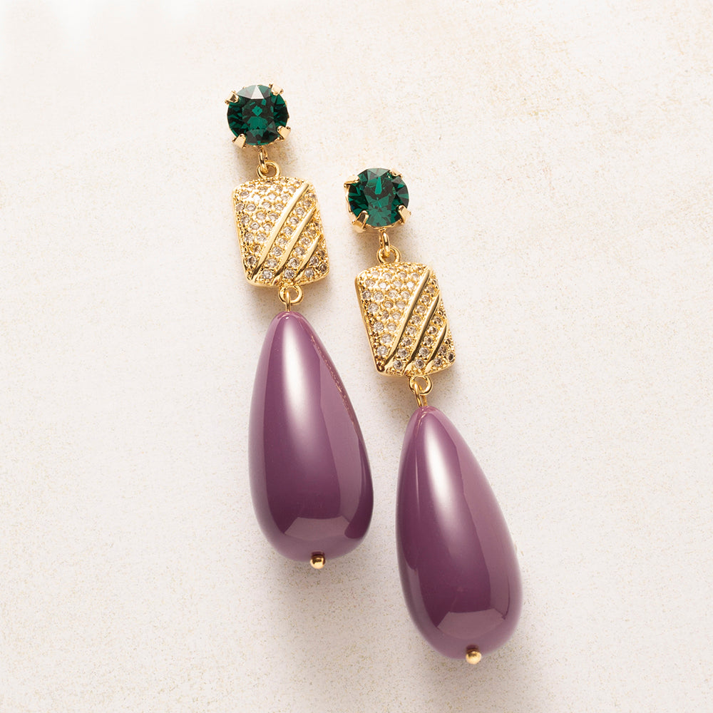 Een diepe aubergine druppel naast een smaragdgroen Swarovski kristal: een kleurcombinatie die opvalt zonder te schreeuwen. Het goudkleurige tussenstuk, bezet met zirkonia, vangt het licht bij elke beweging De gladde, glanzende druppel en de fonkelende steentjes maken deze oorbellen tegelijk verfijnd en krachtig.

Groot in formaat, rustig in kleur: verfijnd genoeg voor kantoor, opvallend genoeg voor een avondje uit.