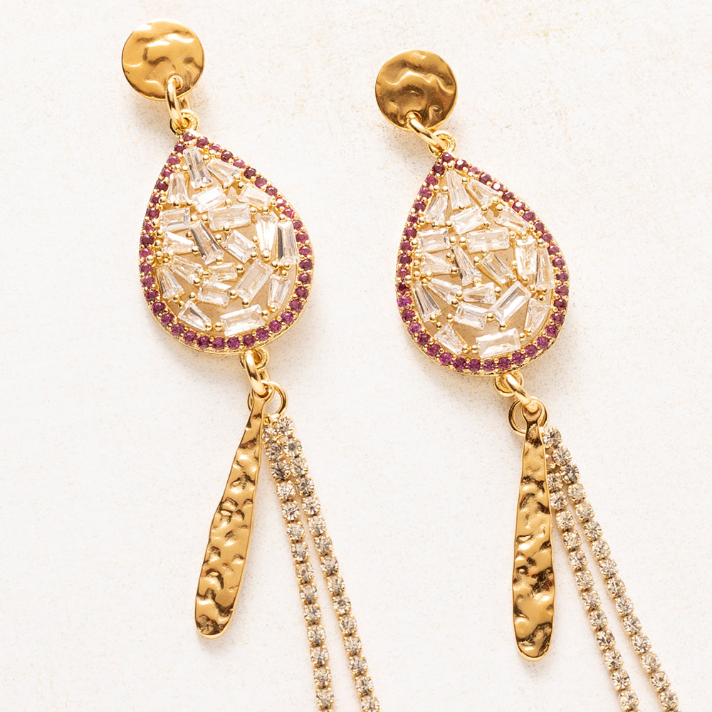 Crystal Cascade is gemaakt om te schitteren. Een druppel vol baguette-geslepen zirkonia, omlijst door een rand van fuchsia steentjes, vormt het hart van het ontwerp. Daaronder hangt een gehamerde gouden staaf naast twee lange zirkonia sliertjes die bij elke beweging het licht vangen.

Het gehamerde goud geeft de oorbellen stoerheid en de zirkonia zorgt voor glamour. Ze hebben weinig nodig om op te vallen: draag ze met je haar opgestoken en een eenvoudige outfit.