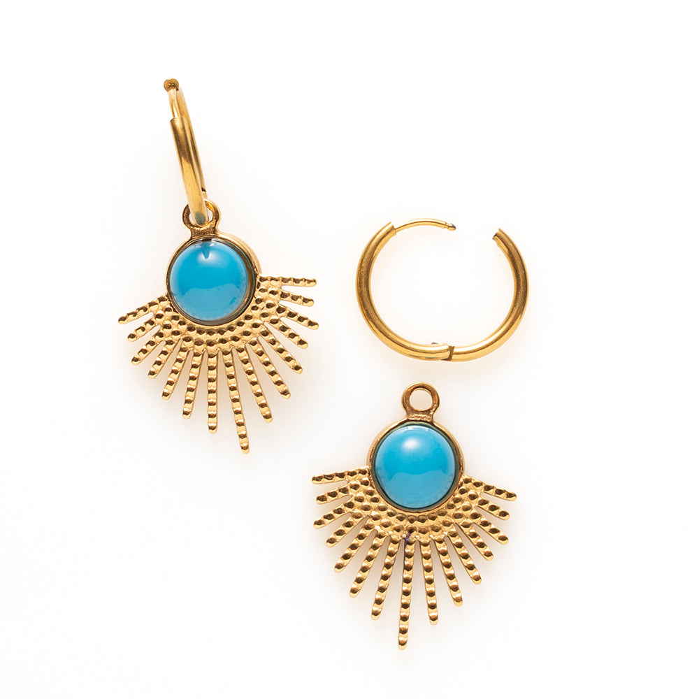 Laat je look stralen met de Azure Sun oorbellen. De gouden hanger waaiert uit als een zonnestraal en draagt in het hart een ronde turkoois in helder blauw, een kleur die meteen opvalt tegen het warme goud. De fijne klapcreool houdt het geheel licht en draagbaar, waardoor deze opvallende vorm net zo goed werkt bij een spijkerbroek als bij een zomerse jurk.