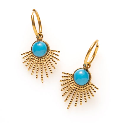 Laat je look stralen met de Azure Sun oorbellen. De gouden hanger waaiert uit als een zonnestraal en draagt in het hart een ronde turkoois in helder blauw, een kleur die meteen opvalt tegen het warme goud. De fijne klapcreool houdt het geheel licht en draagbaar, waardoor deze opvallende vorm net zo goed werkt bij een spijkerbroek als bij een zomerse jurk.