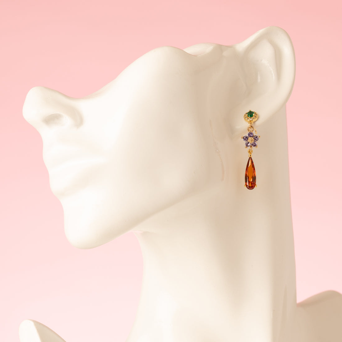 Elegant en speels: Autumn Glow – Flower begint met een groene zirkonia oorsteker, gevolgd door een bloemvormig paars tussenstuk en eindigt in een opvallende oranje druppel van crystal glas. Subtiel van boven, sprankelend van onderen – perfect voor kantoor of een etentje.