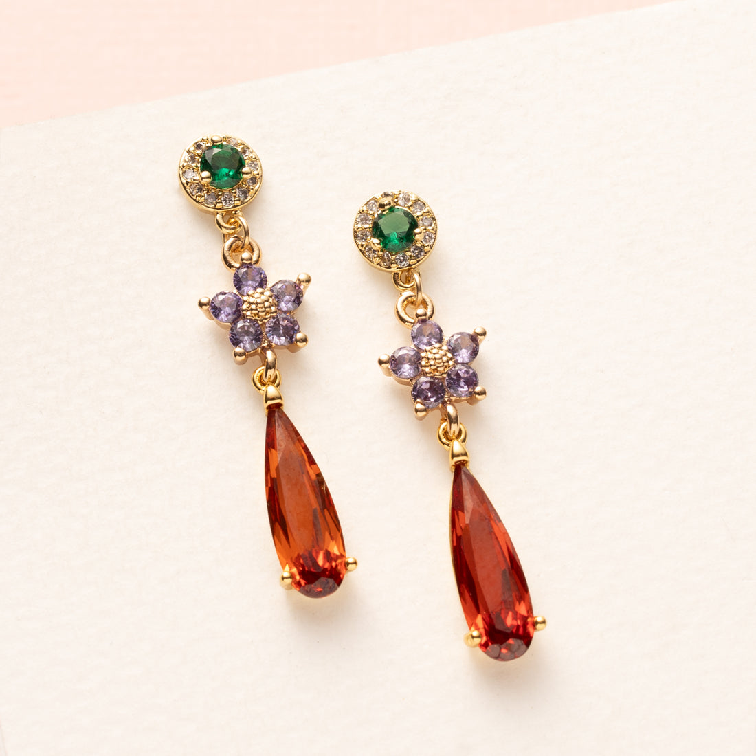 Elegant en speels: Autumn Glow – Flower begint met een groene zirkonia oorsteker, gevolgd door een bloemvormig paars tussenstuk en eindigt in een opvallende oranje druppel van crystal glas. Subtiel van boven, sprankelend van onderen – perfect voor kantoor of een etentje.