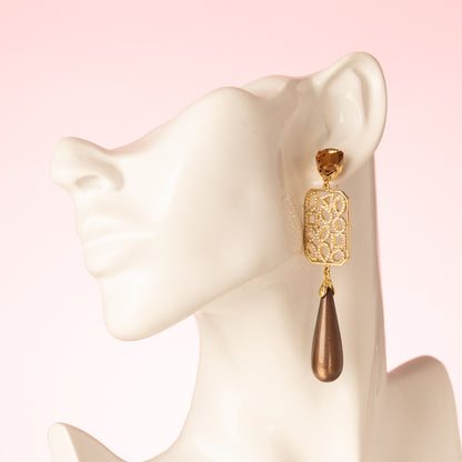 Grand Allure is een spectaculaire statement oorbel die luxe, elegantie en de bruine trendkleur perfect combineert. Kies zelf je stijl met een&amp;nbsp;ronde Swarovski oorsteker of druppelvormige Strass oorsteker in Light Smoked Topaz. Het grote, rechte tussenstuk is versierd met verschillende vormen zirkonia steentjes, en daaronder hangt een glanzende donkerbruine Polaris druppel.

Een oorbel die kracht, glamour en impact uitstraalt – een echte eyecatcher voor vrouwen die durven op te vallen.