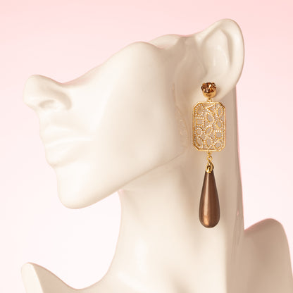 Grand Allure is een spectaculaire statement oorbel die luxe, elegantie en de bruine trendkleur perfect combineert. Kies zelf je stijl met een&amp;nbsp;ronde Swarovski oorsteker of druppelvormige Strass oorsteker in Light Smoked Topaz. Het grote, rechte tussenstuk is versierd met verschillende vormen zirkonia steentjes, en daaronder hangt een glanzende donkerbruine Polaris druppel.

Een oorbel die kracht, glamour en impact uitstraalt – een echte eyecatcher voor vrouwen die durven op te vallen.