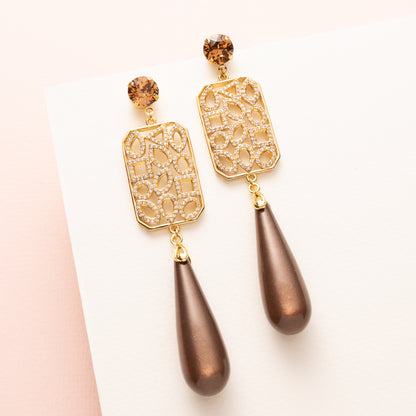 Grand Allure is een spectaculaire statement oorbel die luxe, elegantie en de bruine trendkleur perfect combineert. Kies zelf je stijl met een&amp;nbsp;ronde Swarovski oorsteker of druppelvormige Strass oorsteker in Light Smoked Topaz. Het grote, rechte tussenstuk is versierd met verschillende vormen zirkonia steentjes, en daaronder hangt een glanzende donkerbruine Polaris druppel.

Een oorbel die kracht, glamour en impact uitstraalt – een echte eyecatcher voor vrouwen die durven op te vallen.
