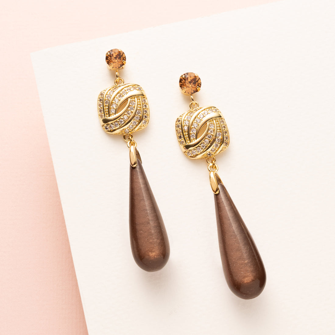 Laat je look stralen met deze elegante oorbellen in warme, rijke bruintinten. De bruine polaris druppels met een zachte glans vallen prachtig samen met het fonkelende vierkante zirkonia tussenstuk en de schitterende Swarovski oorstekers in Light Smoked Topaz. Trendy en vrouwelijk, met een subtiele luxe uitstraling die je zowel overdag als ’s avonds laat opvallen.