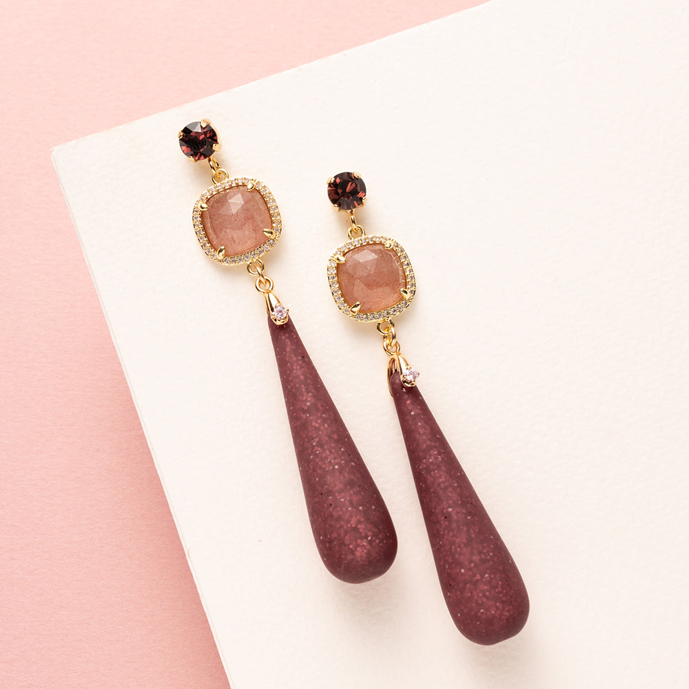 Elegante grote oorbellen, ontworpen om op te vallen. De oorstekers zijn bezet met een schitterende Swarovski puntsteen in de kleur burgundy, terwijl de donkerrode Polaris druppels een diepe, warme gloed toevoegen. De natuurlijke schoonheid van aardbeienkwarts maakt het ontwerp compleet, met een vleugje luxe en verfijning. 
