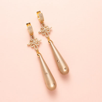 Laat je betoveren door de verfijnde elegantie van Moonlight Grace. Deze statement oorbellen combineren een zachte greige (grijs/bruine) Polaris druppel – subtiel bezet met zes fonkelende Swarovski steentjes – met een schitterend tussenstuk vol zirkonia. De oorbel sluit met elegante zirkonia oorringen die een classy sparkle toevoegen. Groot, opvallend en onweerstaanbaar stijlvol: perfect voor een avond vol allure of een chique diner.