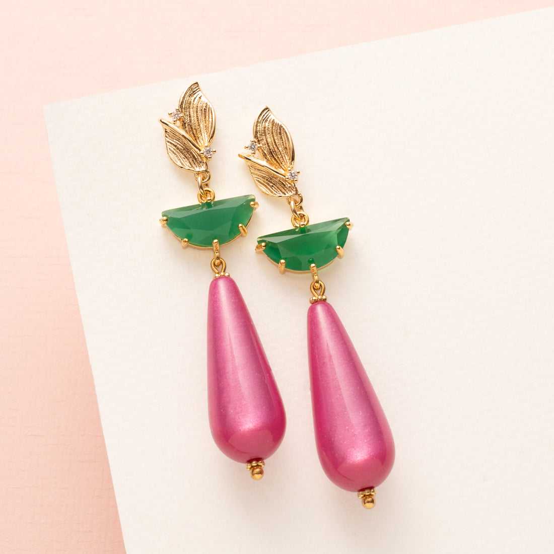Statement oorbellen met een gouden oorsteker in de vorm van een blaadje, subtiel bezet met zirkonia. Het tussenstuk is een groene half ronde hanger van crystal glas, met daaronder een sprankelende fuchsia polaris druppel. Elegant, opvallend en een echte eyecatcher, maar toch stijlvol genoeg voor op kantoor of een chique casual look.