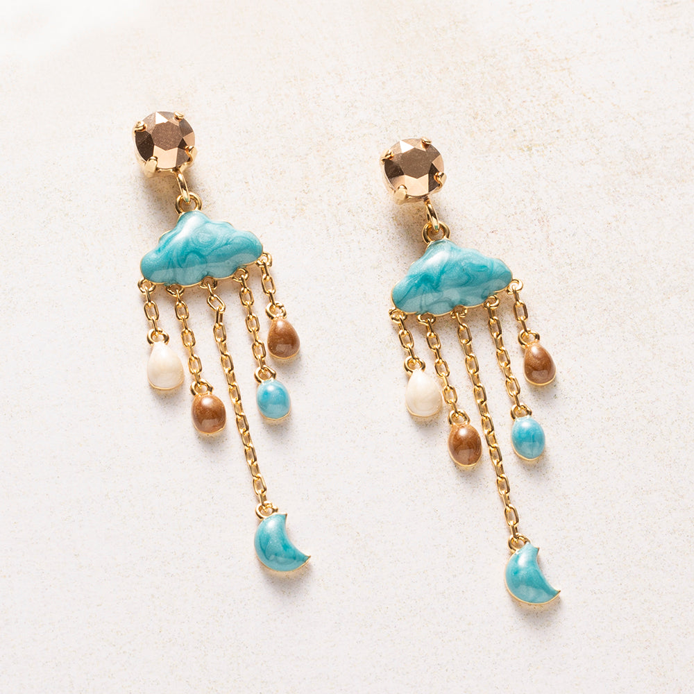 Cloud Nine is een oorbel met een knipoog, maar wel een verfijnde. Onder een Swarovski oorsteker in Crystal Rose Gold hangt een wolkje van turquoise emaille, met fijne gouden kettinkjes eraan. Daaraan hangen druppels in crème, karamel en turquoise, en onderaan een klein maantje.

Door het gemarmerde emaille en de warme kleuren is het ontwerp speels en tegelijk stijlvol. De kettinkjes bewegen mee met elke beweging, of je nu naar kantoor gaat of een avondje uit.