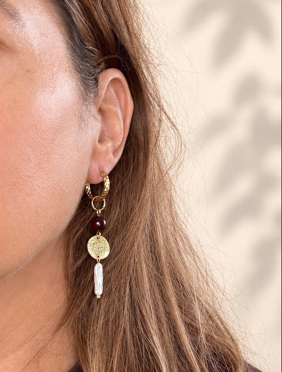 Pearl Rebel combineert stoerheid met elegantie. Het gehamerde goud en de getextureerde plaatjes geven de oorbellen lef en de barokke zoetwaterparels maken ze vrouwelijk. De glanzende two-tone resin kralen in bordeaux/bruin voegen een warm kleuraccent toe.

Het warme bordeaux/bruin geeft diepte en het goud vangt het licht. Zoetwaterparels hebben van nature elk een eigen vorm, dus geen twee paren zijn gelijk. Het asymmetrische ontwerp geeft deze oorbellen uitgesproken karakter. 