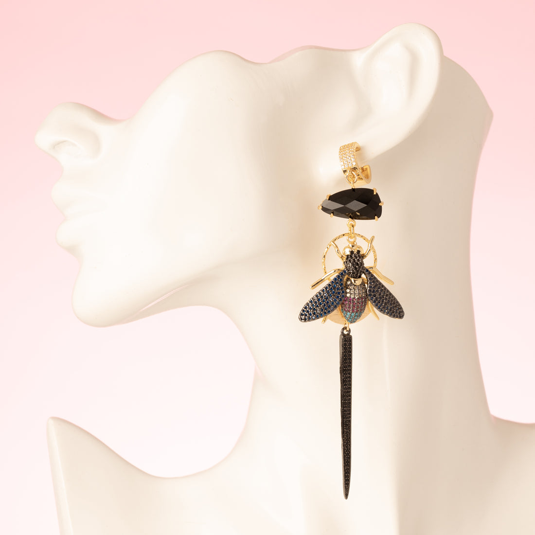 Asymmetrische statement oorbellen met grote zwarte kristalglasstenen, kleurrijke vliegen in donkerblauw, turquoise, magenta en kristal, bezaaid met zirkonia stenen. Gunmetal afwerking voor een stoere, gedurfde look. Gemaakt van 18kt gold plated brass, nikkelvrij, ideaal voor de vrouw die opvalt. Oorbellen met sluitbare ringen.