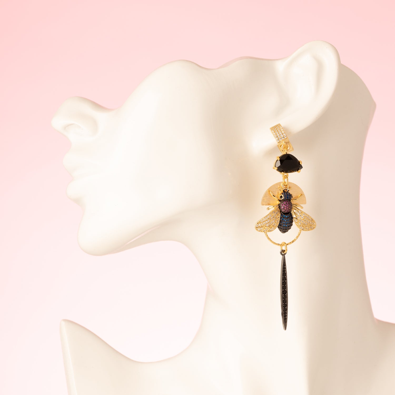 Asymmetrische statement oorbellen met grote zwarte kristalglasstenen, kleurrijke vliegen in donkerblauw, turquoise, magenta en kristal, bezaaid met zirkonia stenen. Gunmetal afwerking voor een stoere, gedurfde look. Gemaakt van 18kt gold plated brass, nikkelvrij, ideaal voor de vrouw die opvalt. Oorbellen met sluitbare ringen.