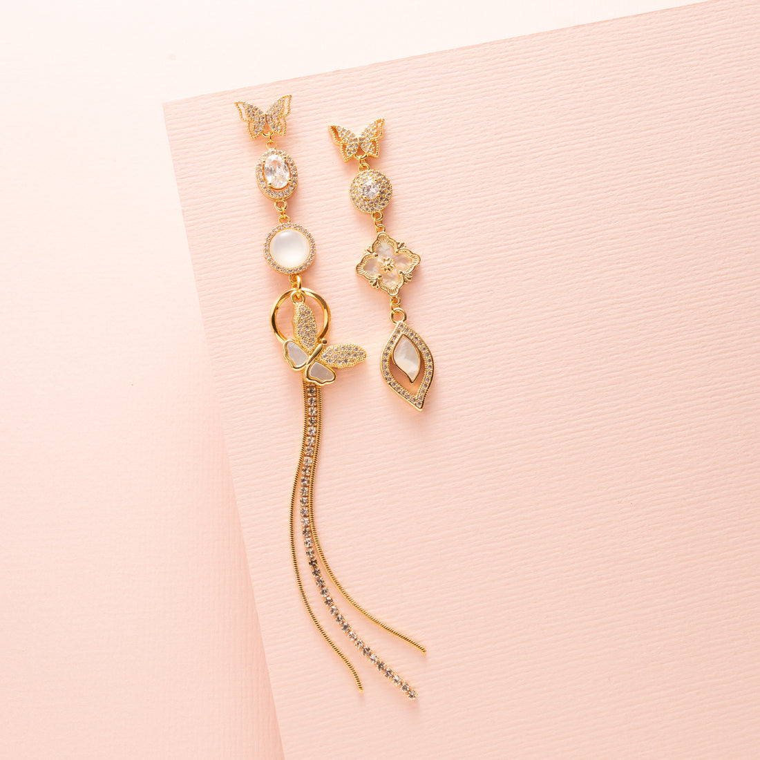Deze prachtige asymmetrische oorbellen zijn een waar statement. De stekers zijn in de vorm van een elegante vlinder, die een verfijnde en delicate uitstraling geeft. De oorbellen zijn verder versierd met schitterende zirkonia en parelmoer stenen, wat zorgt voor een luxe en sprankelend effect. Een subtiele fringe van zirkonia steentjes voegt een speels en sierlijk element toe aan het geheel.