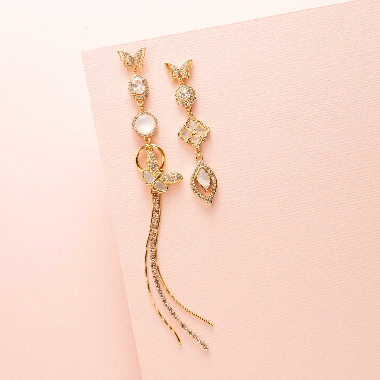 Deze prachtige asymmetrische oorbellen zijn een waar statement. De stekers zijn in de vorm van een elegante vlinder, die een verfijnde en delicate uitstraling geeft. De oorbellen zijn verder versierd met schitterende zirkonia en parelmoer stenen, wat zorgt voor een luxe en sprankelend effect. Een subtiele fringe van zirkonia steentjes voegt een speels en sierlijk element toe aan het geheel.
